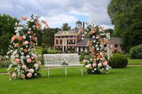 foto van twee bloembogen met oranje en witte bloemen op een grasveld. op de achtergrond is een kasteel te zien